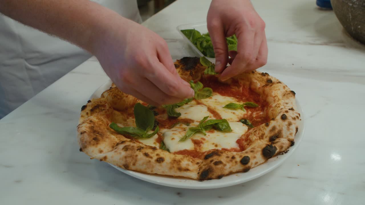 Adding Basel leaves onto freshly baked Neapolitan pizza with mozzarella cheese