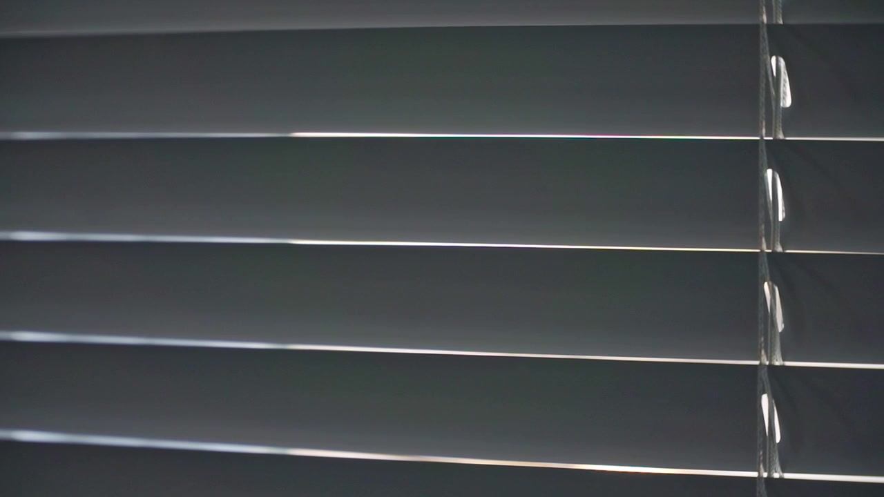 Horizontal blinds swaying over a window, reducing sunlight and enhancing privacy. Perfect for residential, office, and architectural stock footage.