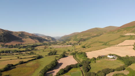 wide shot aerial drone footage rising up over a welsh valley surrounded by farmers fields on a bright sunny day