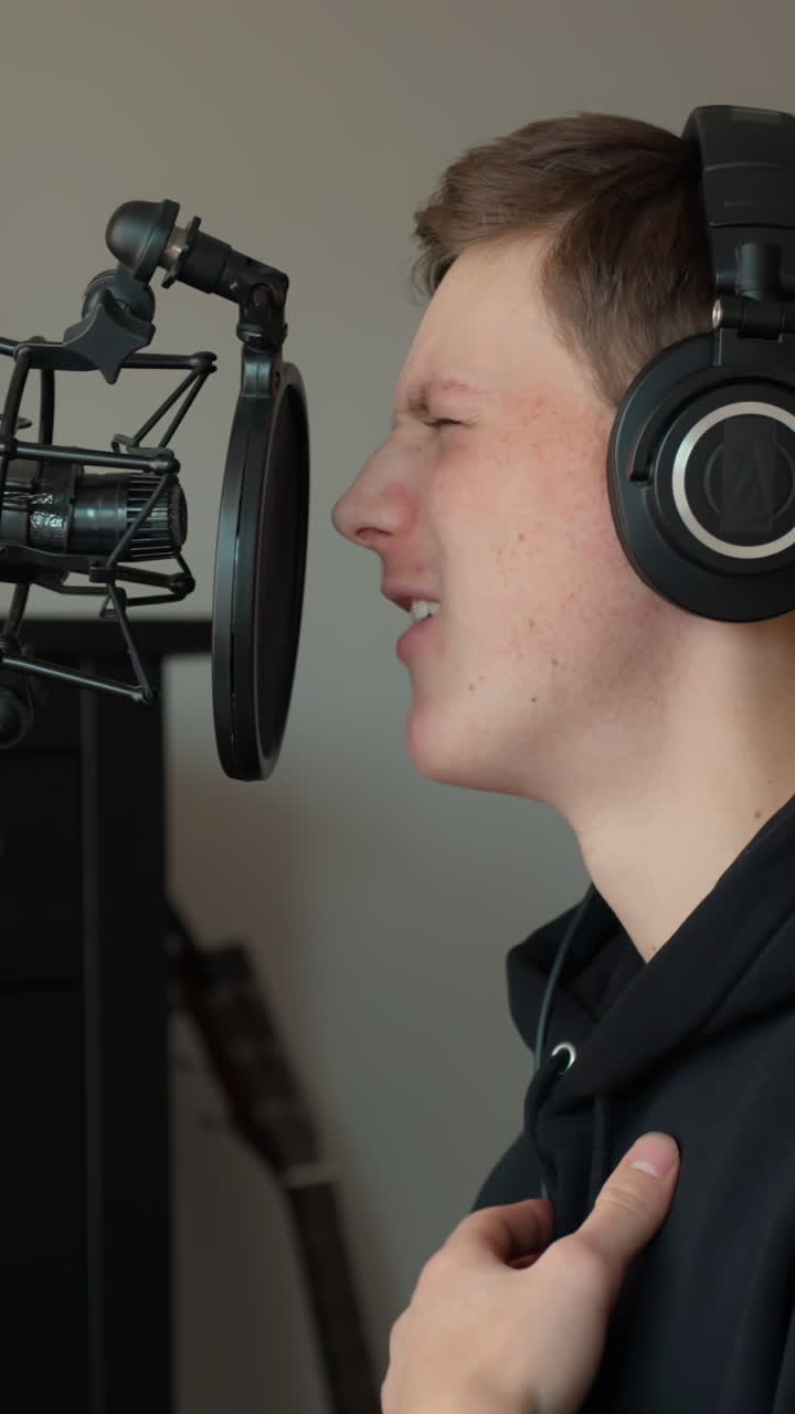 Giovane produttore musicale che registra parti vocali in uno studio domestico con un microfono e un'espressione concentrata, canto verticale