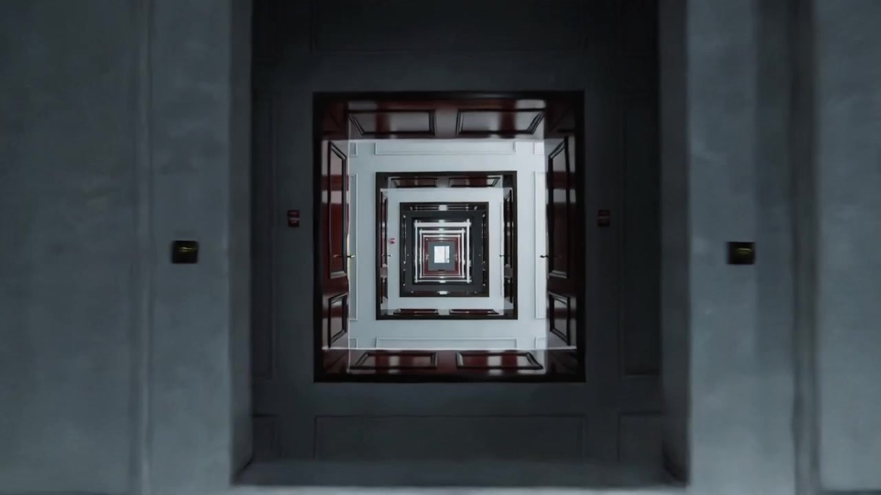 Un dolly inizia ad allontanare la telecamera per rivelare un atrio incassato nella tromba delle scale, mostrando porte in legno.