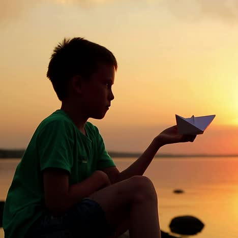 boy with paper boat at sunset