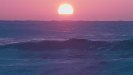 tranquil sea waves break in the foreground as the red sun sets in the background