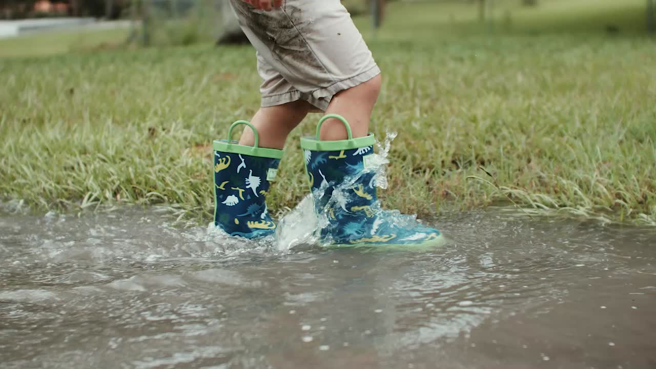 A young child walking in a rain puddle with rain boots