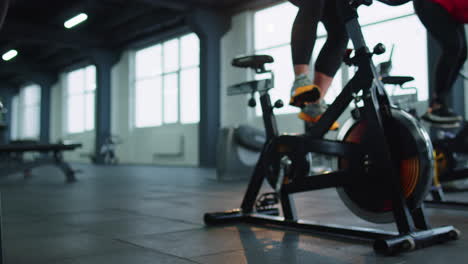 Close-up-legs-of-group-unrecognizable-friends-at-gym-exercising-on-stationary-bike-at-class-in-gym