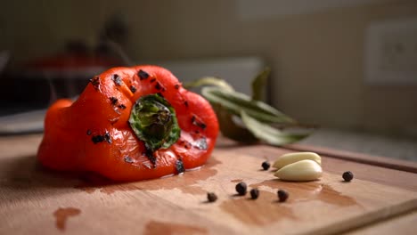 roasted red bell pepper on wooden board with black peppercorns and peeled garlic