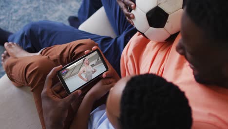 composite of father and son at home watching athletics event on smartphone
