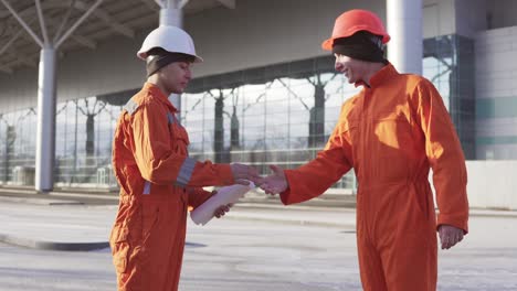Director-of-the-project-examining-the-building-object-with-construction-worker-in-orange-uniform-and-helmet.-They-meeting-each-other-at-the-bulding-object-and-shaking-hands.