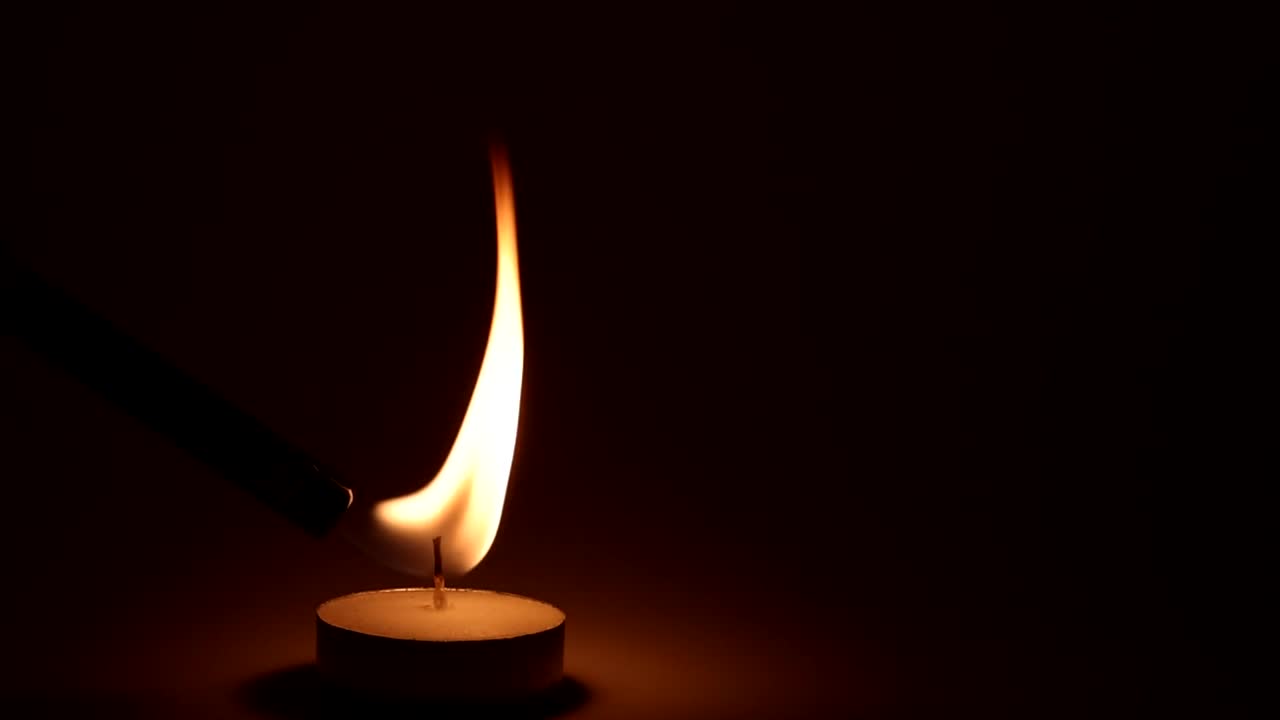 A detailed view of a candle flame flickering gently, casting a warm glow in the surrounding darkness.