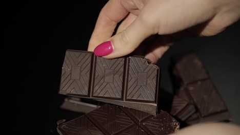 woman breaks black chocolate bar. close-up. slow motion