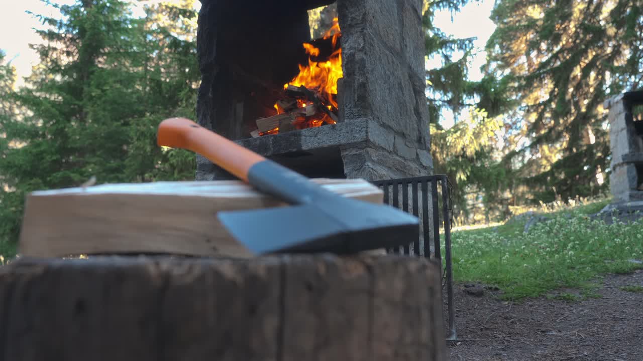 Fire burning in a stone outdoor fireplace with an axe in the foreground