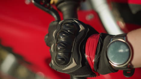 close-up of a biker's hand wearing black protective gloves while holding a motorcycle clutch lever with two fingers, a smartwatch is visible on the wrist