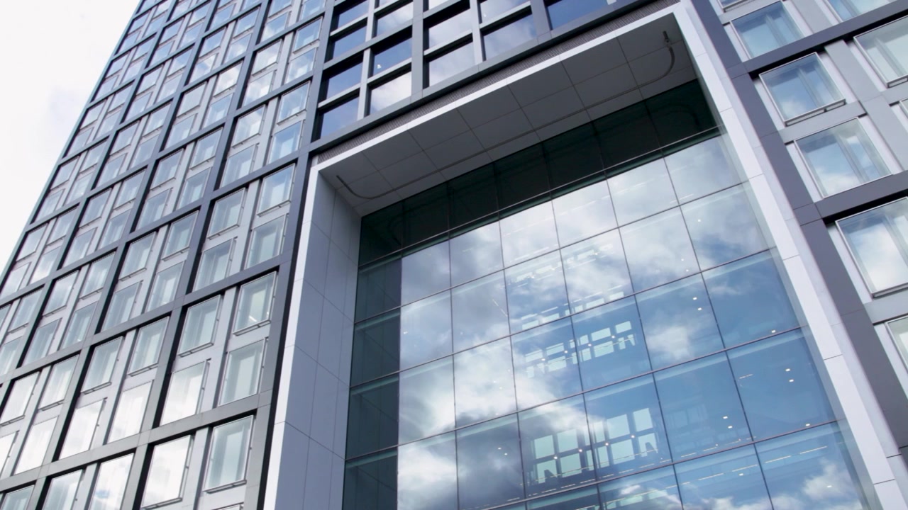 Le nuvole si riflettono nelle finestre di vetro di un alto edificio moderno per uffici o appartamenti.