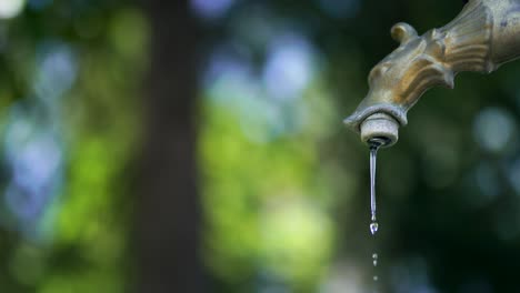 corriente ligera de agua cristalina que desemboca lentamente desde el grifo de hierro. pequeñas gotas de agua azul que caen desde el gripo bronceado, movimiento abstracto del agua. sistema de hidratación en ecología