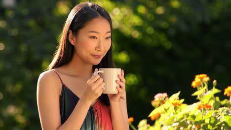 a woman enjoying a serene moment outdoors, holding a warm cup of beverage while surrounded by vibrant flowers, basking in the gentle sunlight and tranquility of nature