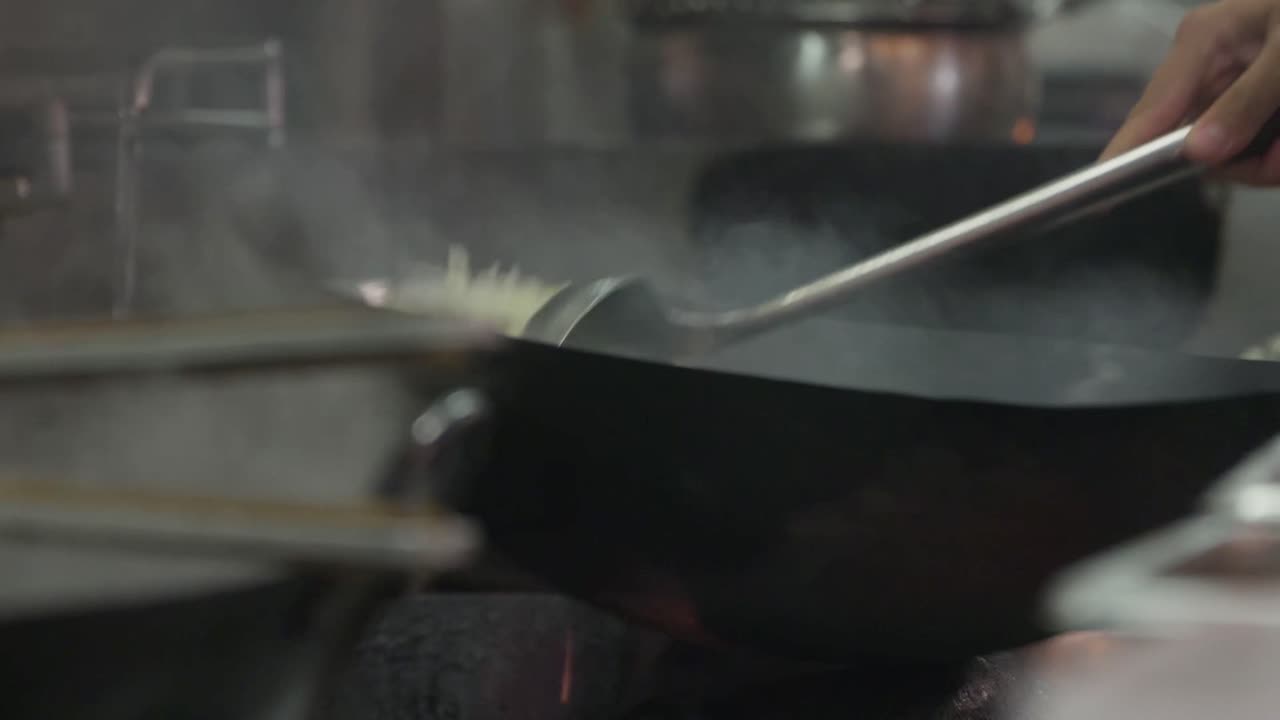 Uno chef giapponese salta il riso fritto in un wok caldo con il suo mestolo in acciaio inossidabile.