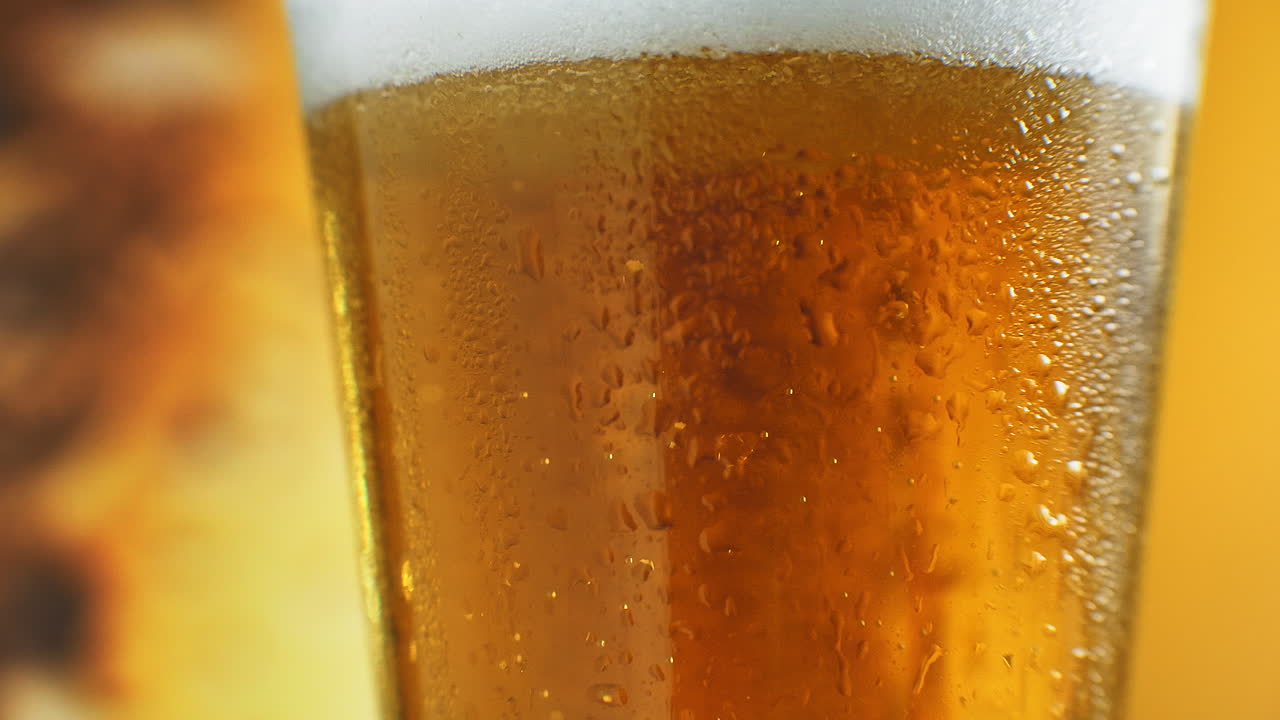 Beer is pouring into angled glass. IPA on tap. Cold Light Beer in a glass with water drops. Craft Beer forming waves close up. Freshness and froth. Bar background. Microbrewery craft beer.