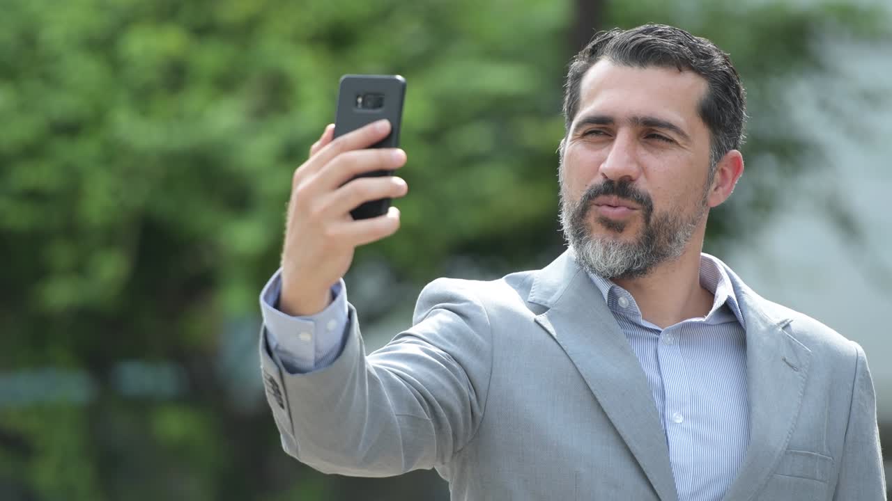 apuesto hombre de negocios persa barbudo tomando selfies en las calles al aire libre