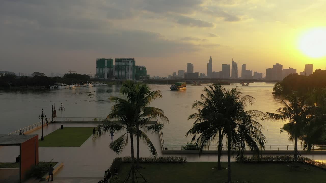 hermosa escena tropical del parque de la puesta del sol desde un dron con personas que disfrutan de actividades de ocio como patinar, correr y andar en bicicleta y vistas al horizonte de la ciudad, a los barcos y al río
