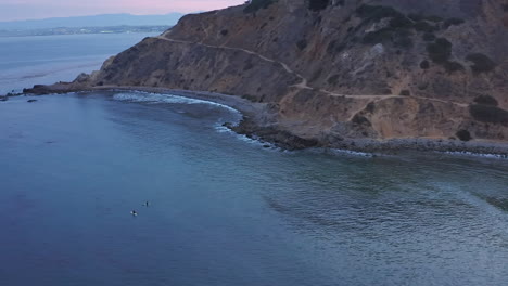 surfers sit on their longboards and wait for the perfect wave at sunset - aerial view of rancho palos verdes bluff and beach