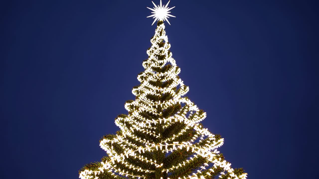 Low-angle shot of a Christmas tree adorned with spiral lights against a dark sky, creating a festive