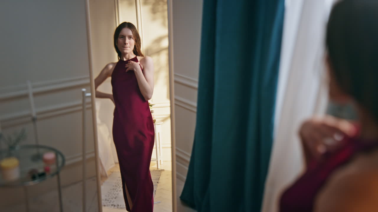 행복한 소녀는 드레스를 입고 거울을 바라보고 있습니다. 매력적인 은 모델이 머리카락을 조정합니다.