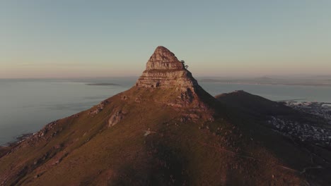 el dron vuela lentamente hacia el pico de la montaña de la cabeza del león - están iluminados por la puesta de sol - en el valle se puede ver ciudad del cabo, sudáfrica - vista del mar abierto