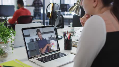 Caucasian-woman-having-a-video-call-on-laptop-with-female-colleague-at-office