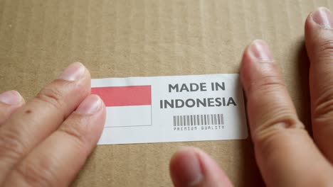 Hands-applying-MADE-IN-INDONESIA-flag-label-on-a-shipping-box-with-product-premium-quality-barcode