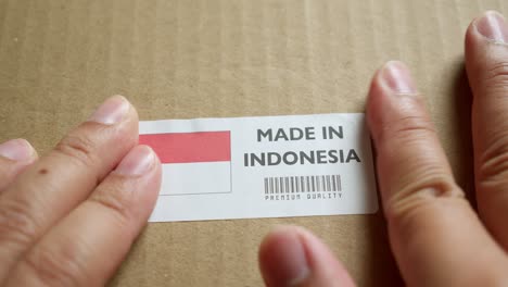 hands applying made in indonesia flag label on a shipping box with product premium quality barcode