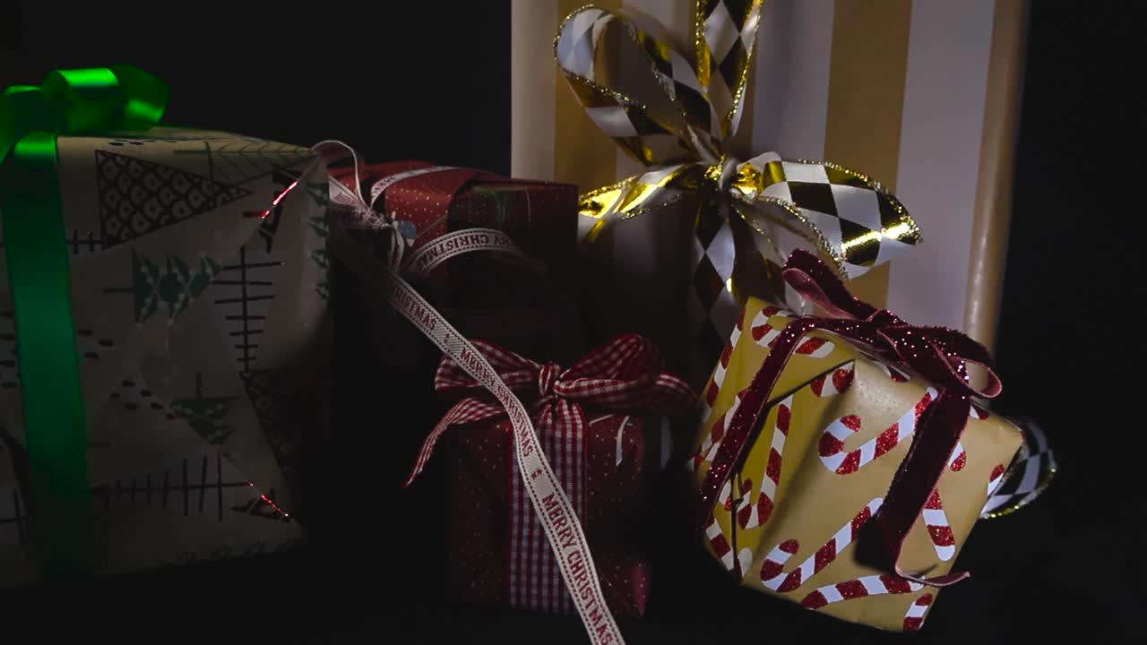 Gorgeous wrapped Christmas presents or holiday gifts with fun candy cane wrapping paper and shiny colorful ribbons in front of a black studio background, shallow depth of field, bokeh background