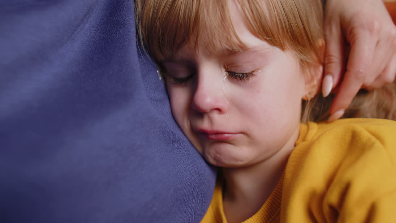 Upset child little girl kid crying with tears flowing down on cheek toddler lies on mother at home