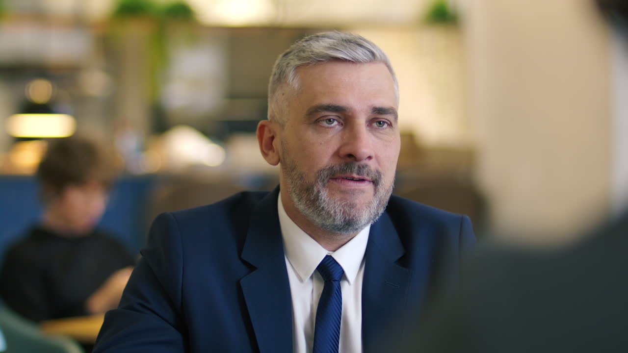 Mid-Aged Businessman Explaining Project Details to Partner at Meeting in Cafe