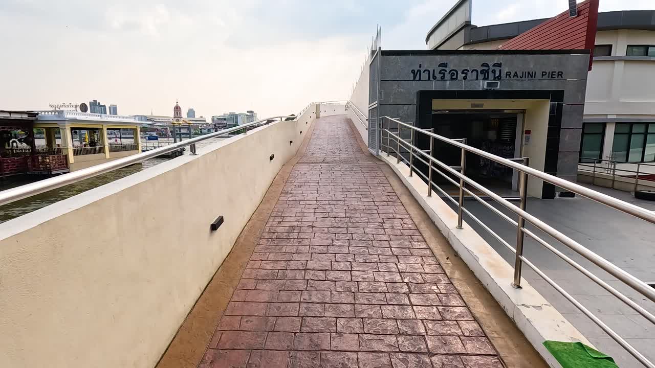 A scenic walk along a riverside pier in Bangkok, Thailand, showcasing urban architecture and river views under natural daylight