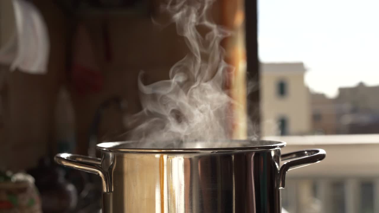 cocción al vapor y cocción de agua en una estufa de calefacción moderna en la cocina en el fondo de un balcón abierto. cocción con vapor emitido por una olla de cocción inoxidable. efectos de evaporación en el aire