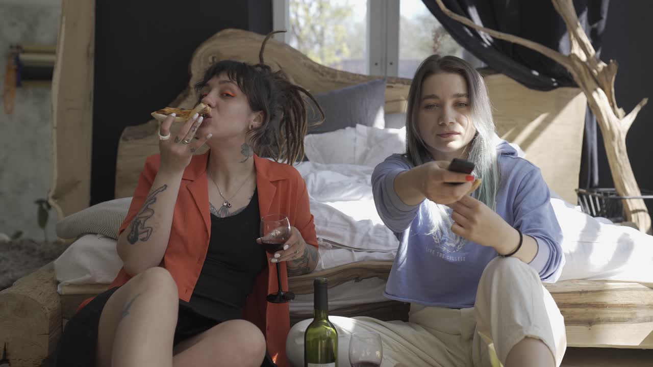 바닥에 앉아 tv를 보면서 와인을 마시고 피자를 먹는 행복한 두 소녀의 앞모습