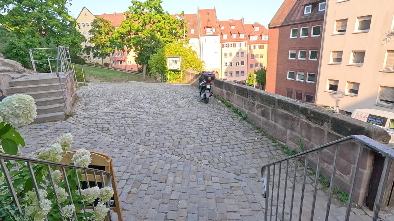 Person exits wooden door onto sunlit cobblestone street with historic buildings in Nuremberg, Germany