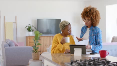 Happy-diverse-female-lesbian-couple-talking-and-using-tablet-with-documents-in-slow-motion