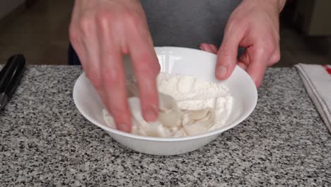 manos cubriendo anillos de calamares crudos con mezcla de harina en un tazón