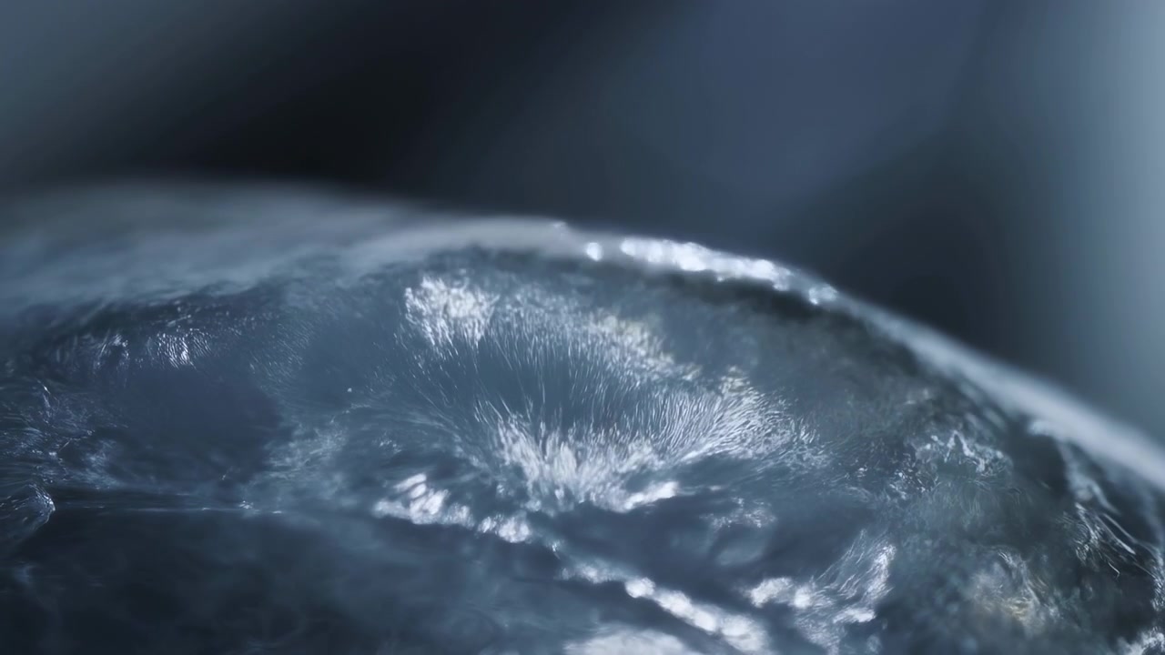 Una vista ravvicinata mostra dettagli di una superficie ghiacciata con riflessi luminosi e un leggero movimento dell'acqua sotto strati ghiacciati testurizzati, catturando toni freddi, riflessi e un ambiente esterno calmo.
