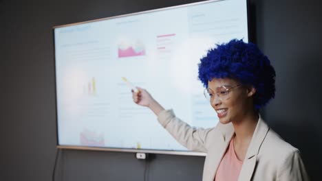 biracial casual businesswoman with blue afro making presentation in office, slow motion