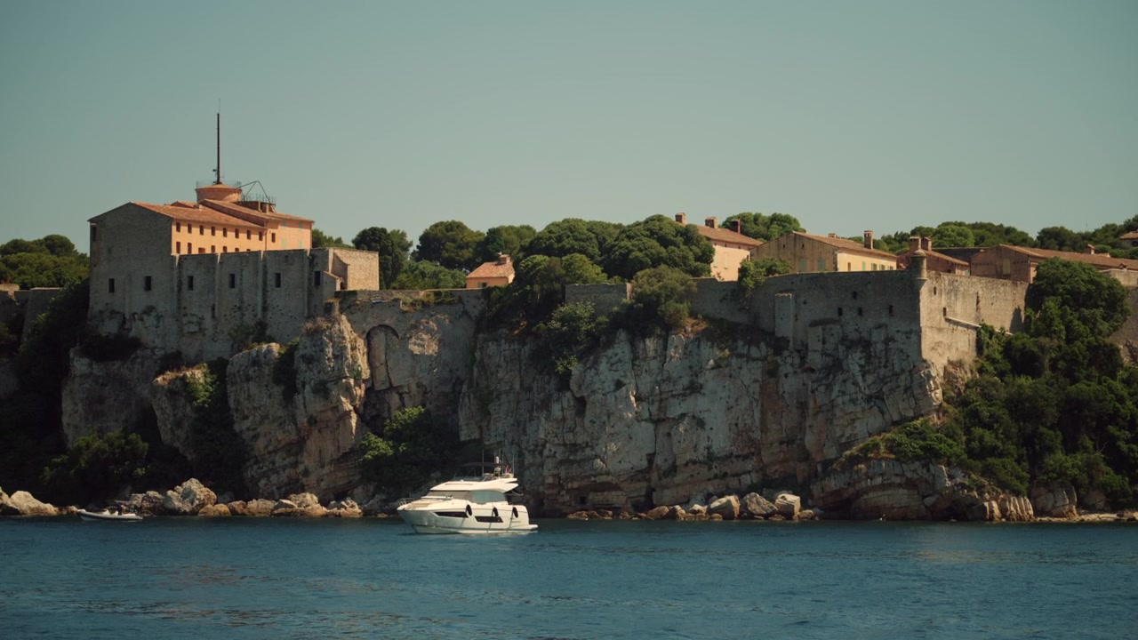 Fortezza storica Fort Royal situata su scogliere rocciose dell'isola di Santa Margherita con uno yacht di lusso che naviga su tranquille acque mediterranee