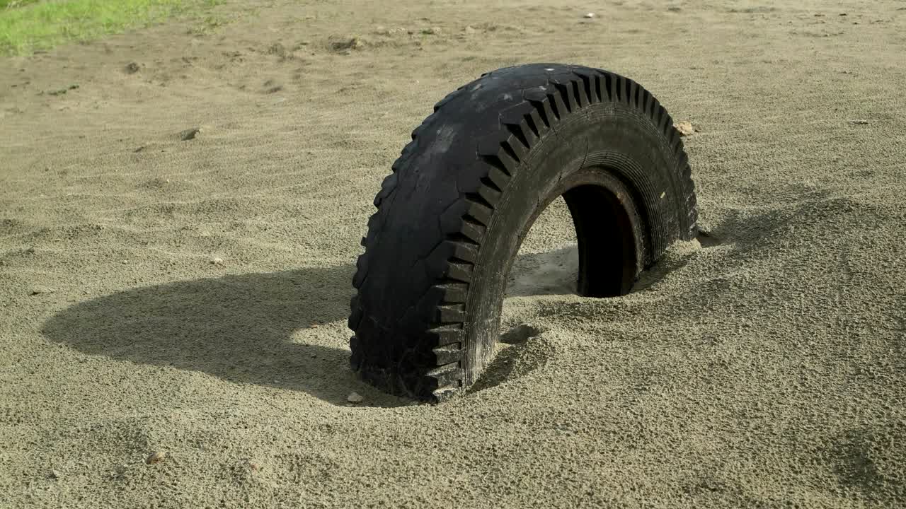 старое колесо машины, похороненное в песке, скользит с глазами на шину.