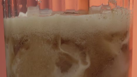 vista en primer plano de un vaso lleno de hielo mientras un camarero vierte una bebida gaseosa de cola carbonatada, las gotas caen en cascada y forman burbujas, capturando la vibrante atmósfera de un bar mexicano