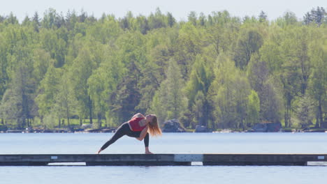 Mujer-Caucásica-Hace-Rutina-De-Flujo-De-Yoga-En-Un-Embarcadero-Flotante-De-Madera-En-El-Lago