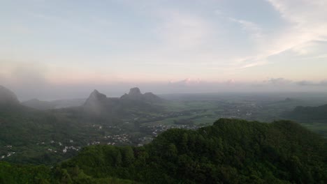 Misty-sunrise-over-the-lush-mountains-of-Verdun,-Mauritius,-with-serene-sky