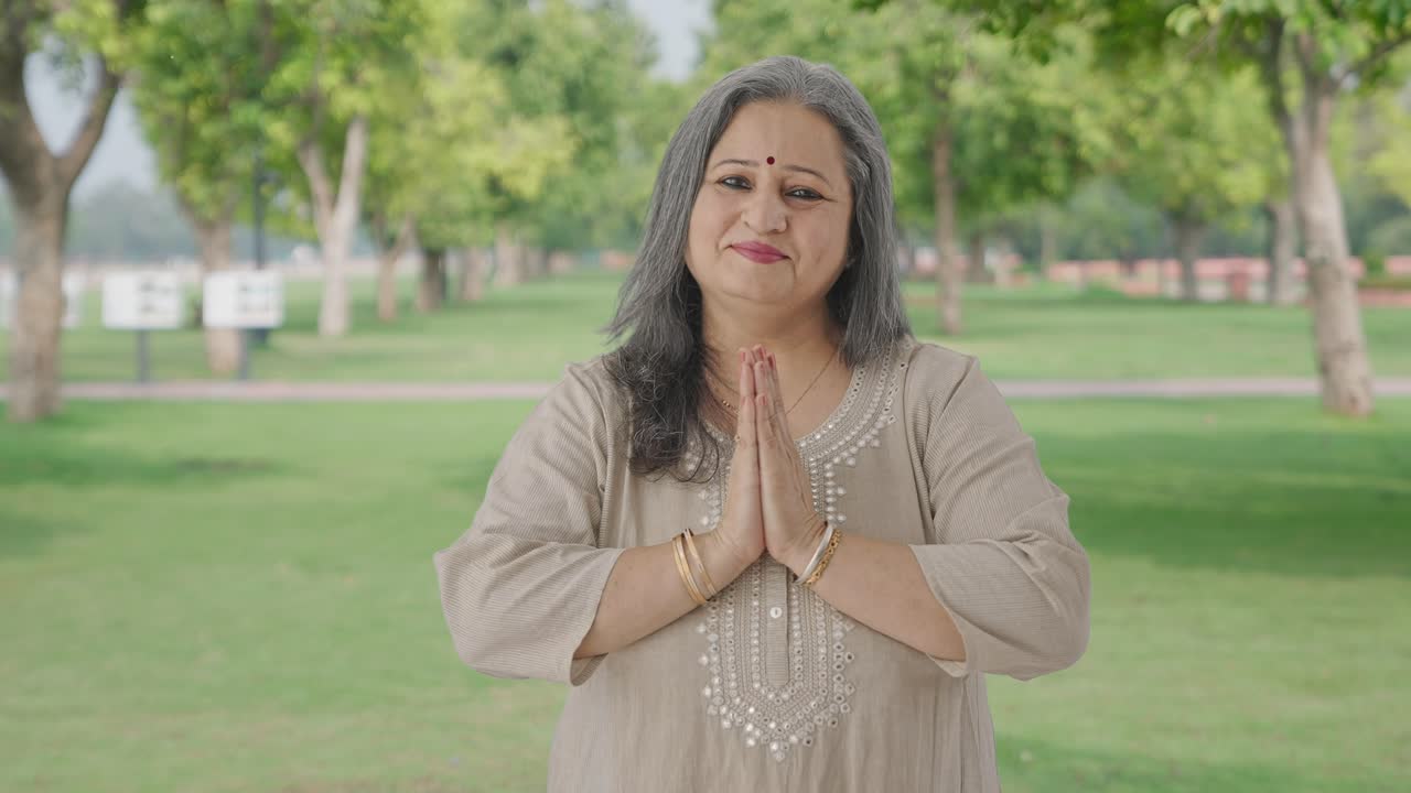 Glückliche ältere Inderin grüßt und macht Namaste im Park.