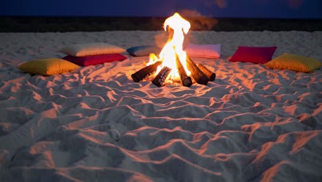 bonfire burning brightly on a sandy beach at dusk, surrounded by colorful cushions, creating a warm and inviting atmosphere perfect for relaxation and gatherings with friends and family
