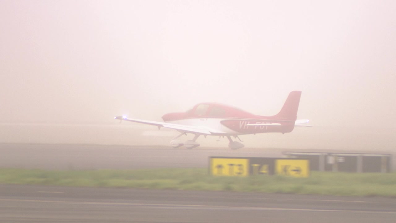 Un piccolo aereo a elica rosso e bianco atterra su una pista bagnata, creando uno spruzzo d'acqua durante una giornata piovosa. Sfide dell'aviazione in condizioni meteorologiche avverse.