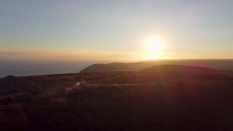 amazing aerial drone shot of sunrise of coastal cliffs with winding hiker path rock cairn and foggy mountains in distance holdstone down exmoor devon uk 4k